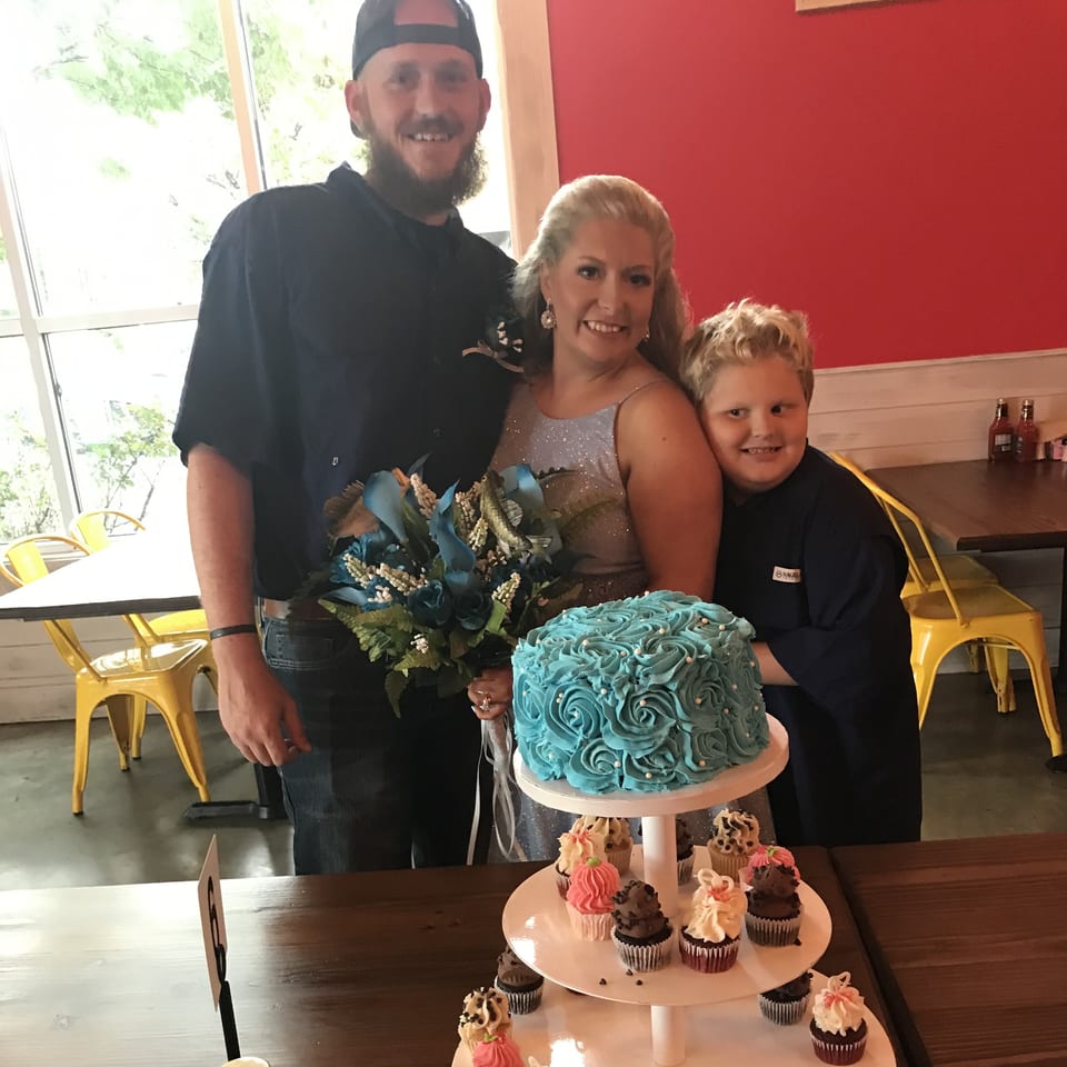 A family of three, with a blue cake and cupcakes, celebrating at Southern BBQ Hilltop.