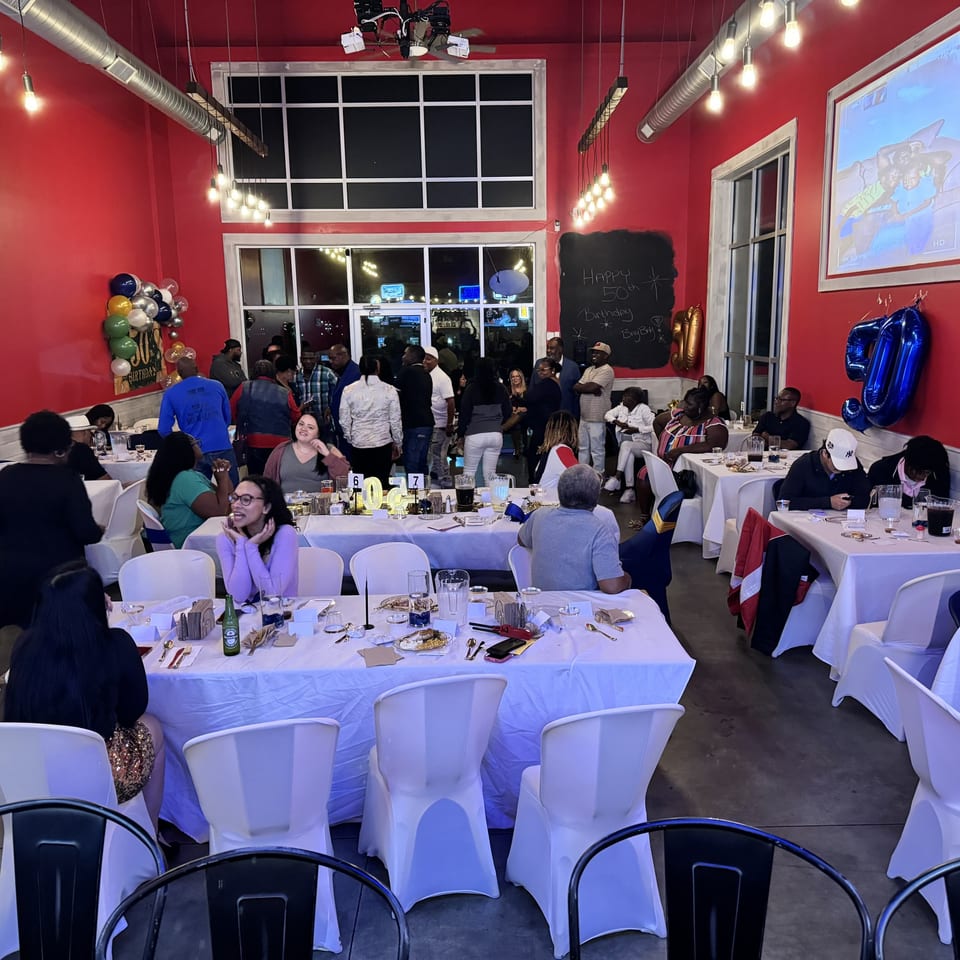 Guests gather in a red-walled Southern BBQ Hilltop dining room with white-clothed tables and balloons.