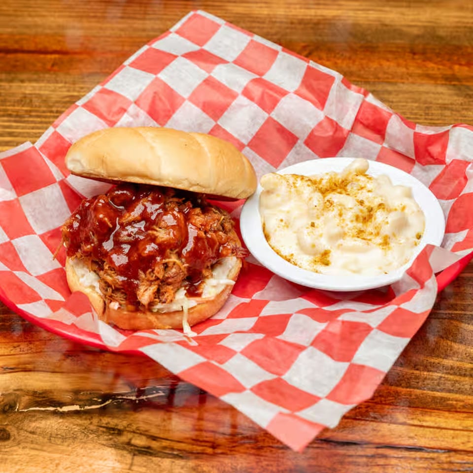 BBQ pulled pork sandwich with coleslaw and mac and cheese, served in a red checkered basket.