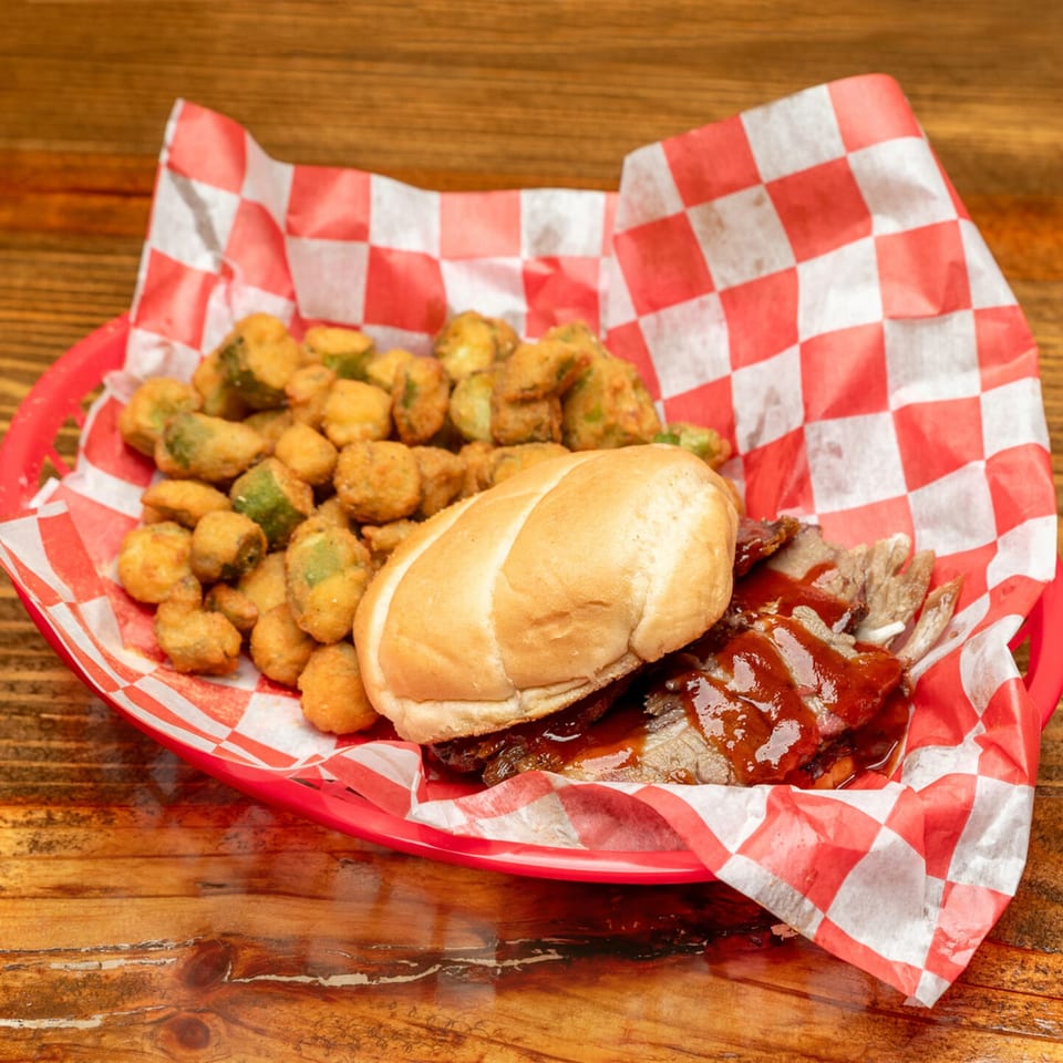 Southern BBQ Hilltop's brisket sandwich with BBQ sauce and a side of fried okra in a red basket.