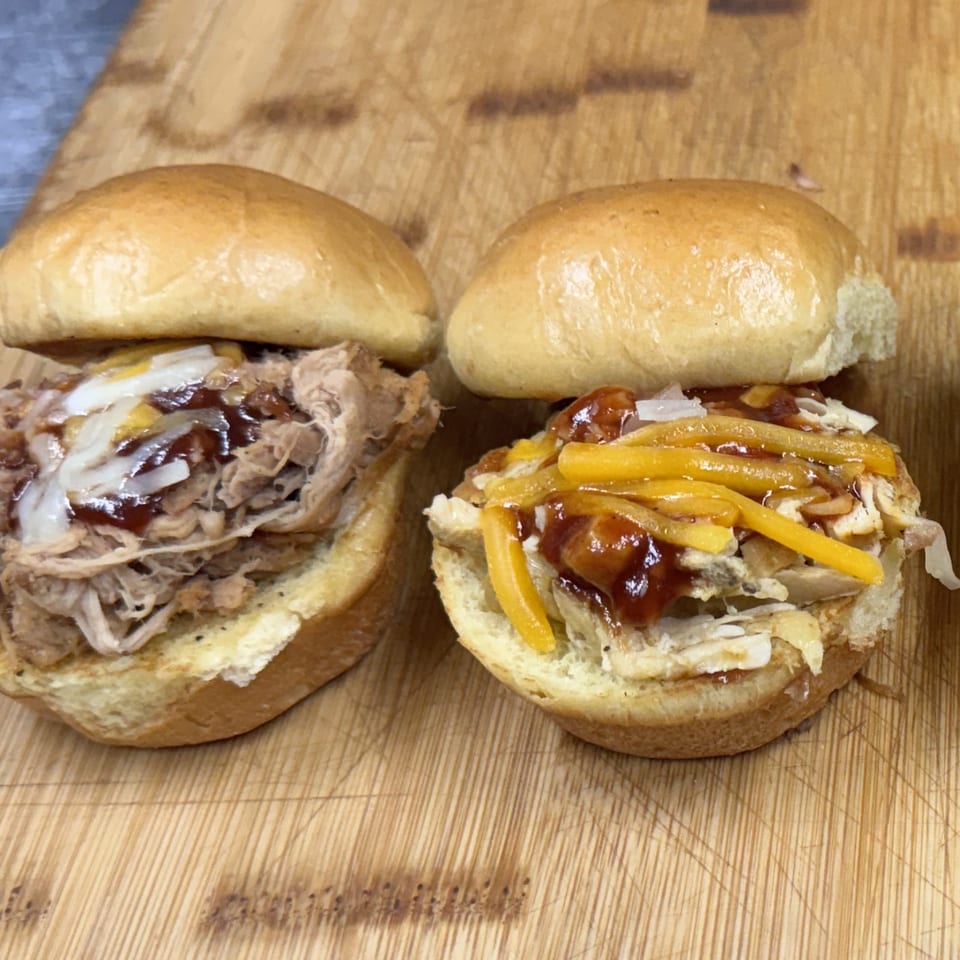 Two Southern BBQ Hilltop sliders on a wooden board, one pulled pork, one chicken with cheese.